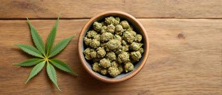 Was sind CBD Blüten: getrocknete CBD Blüten in einer Keramikschale neben einem Hanfblatt auf Holz
